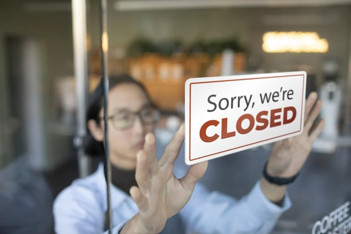 A sign indicating that the business is closed is being installed by an employee